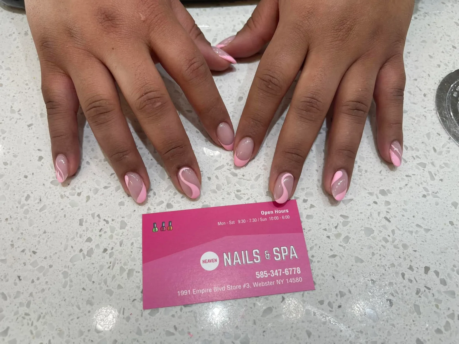 Pink swirl French tips on almond nails, with a Heaven Nails & Spa card on the counter